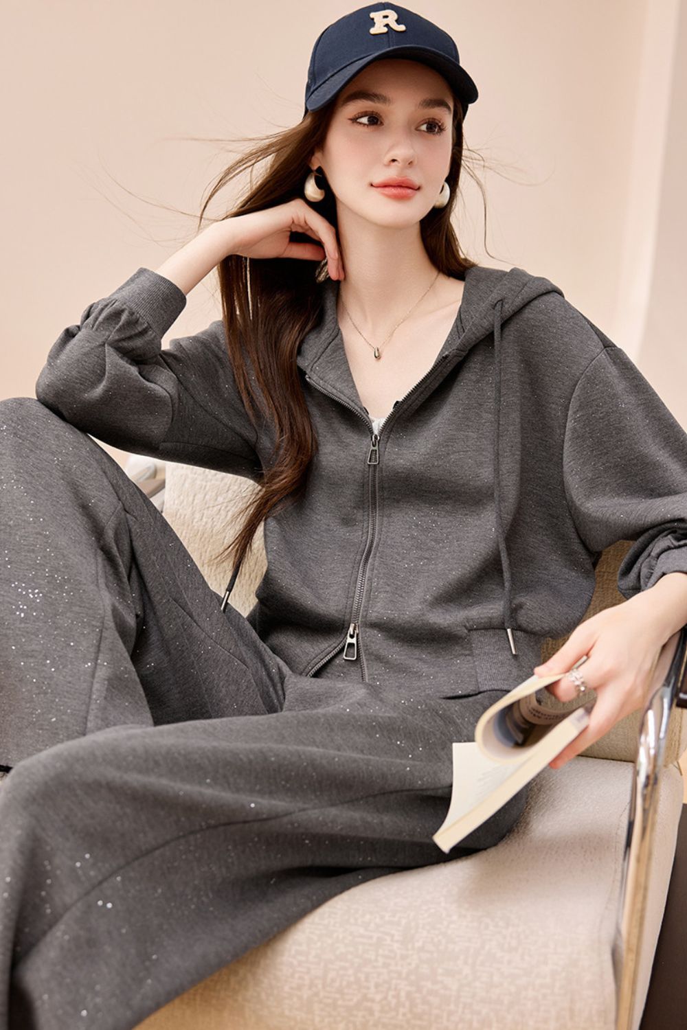 Seated model in gray wide-leg jumpsuit with collar detail, styled with a navy cap