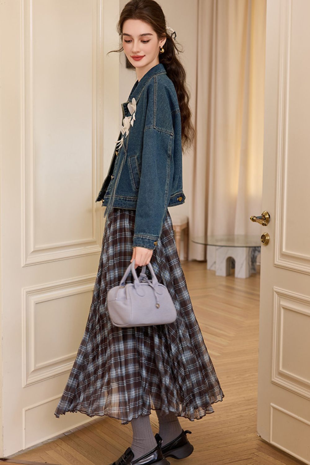 Side view of woman in denim jacket with floral appliqué and plaid skirt, holding a gray handbag