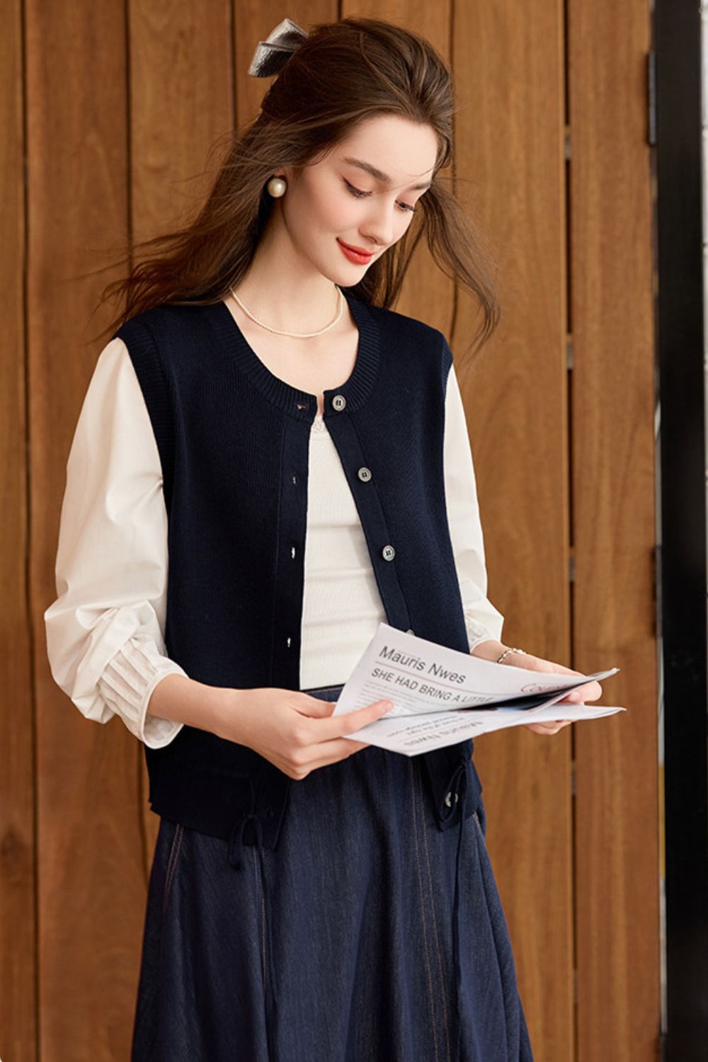 Full-length view of model in navy blue knit vest with long skirt and blouse, holding a book