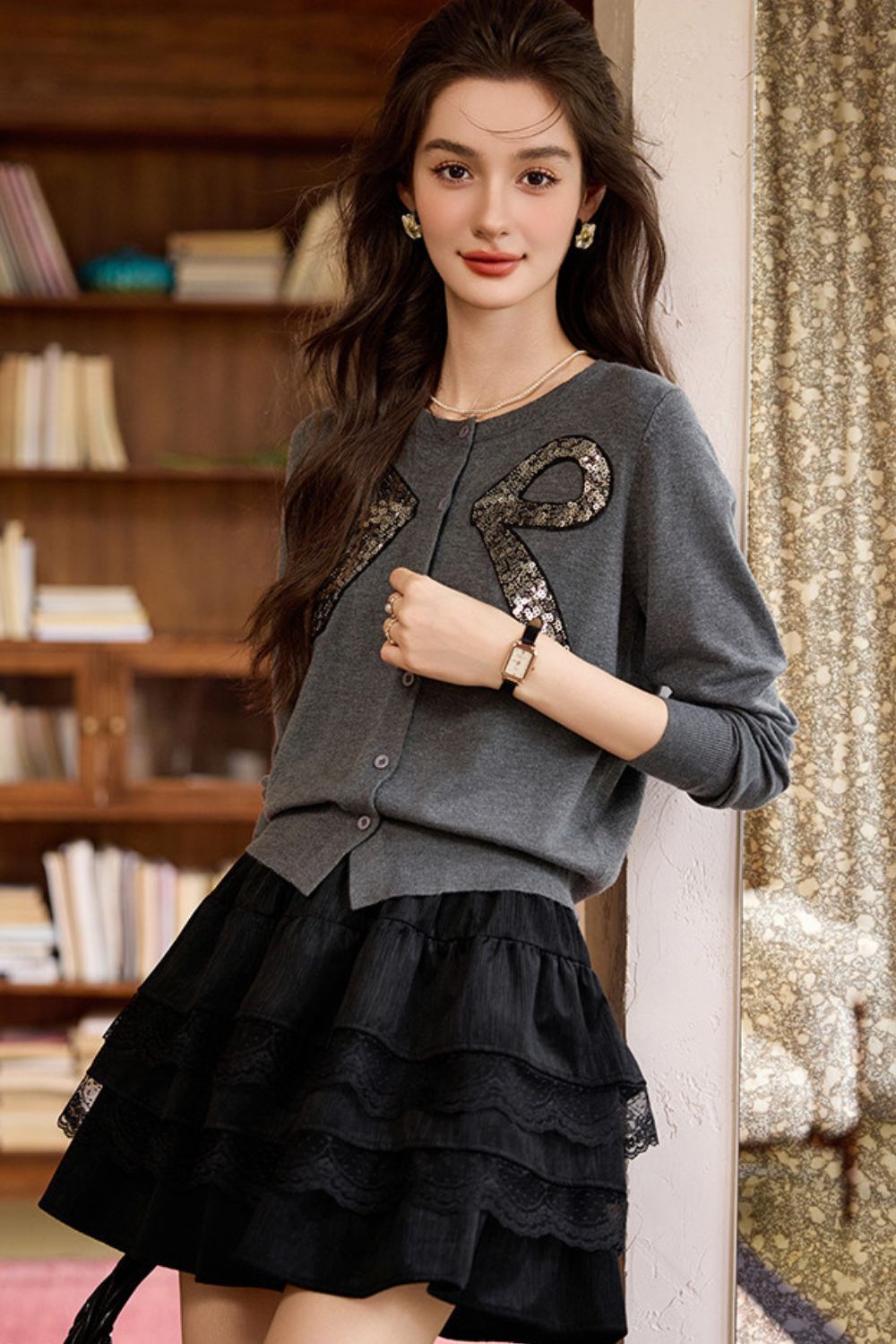 Model wearing a gray embellished sweater with bow details paired with a black layered ruffle skirt