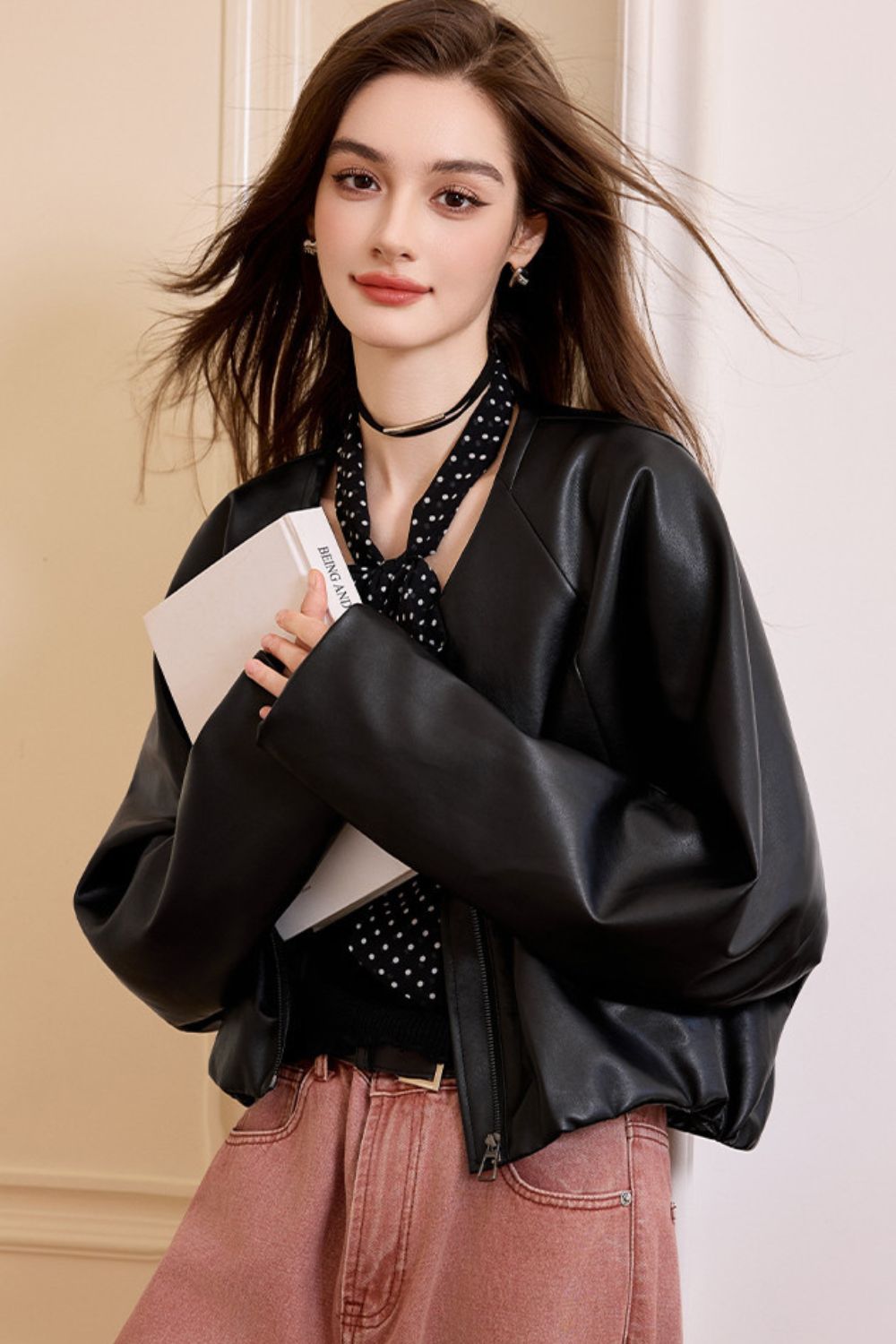 Front view of woman wearing a black faux leather jacket over a polka dot blouse with pink pants