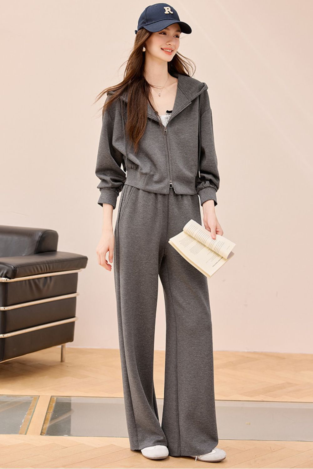 Model wearing a casual gray wide-leg jumpsuit with a collar, paired with a navy cap and white clutch bag