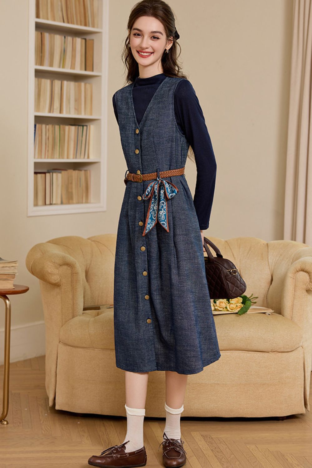 Model wearing a navy long-sleeve button-front denim midi dress with a brown belt, standing in a living room