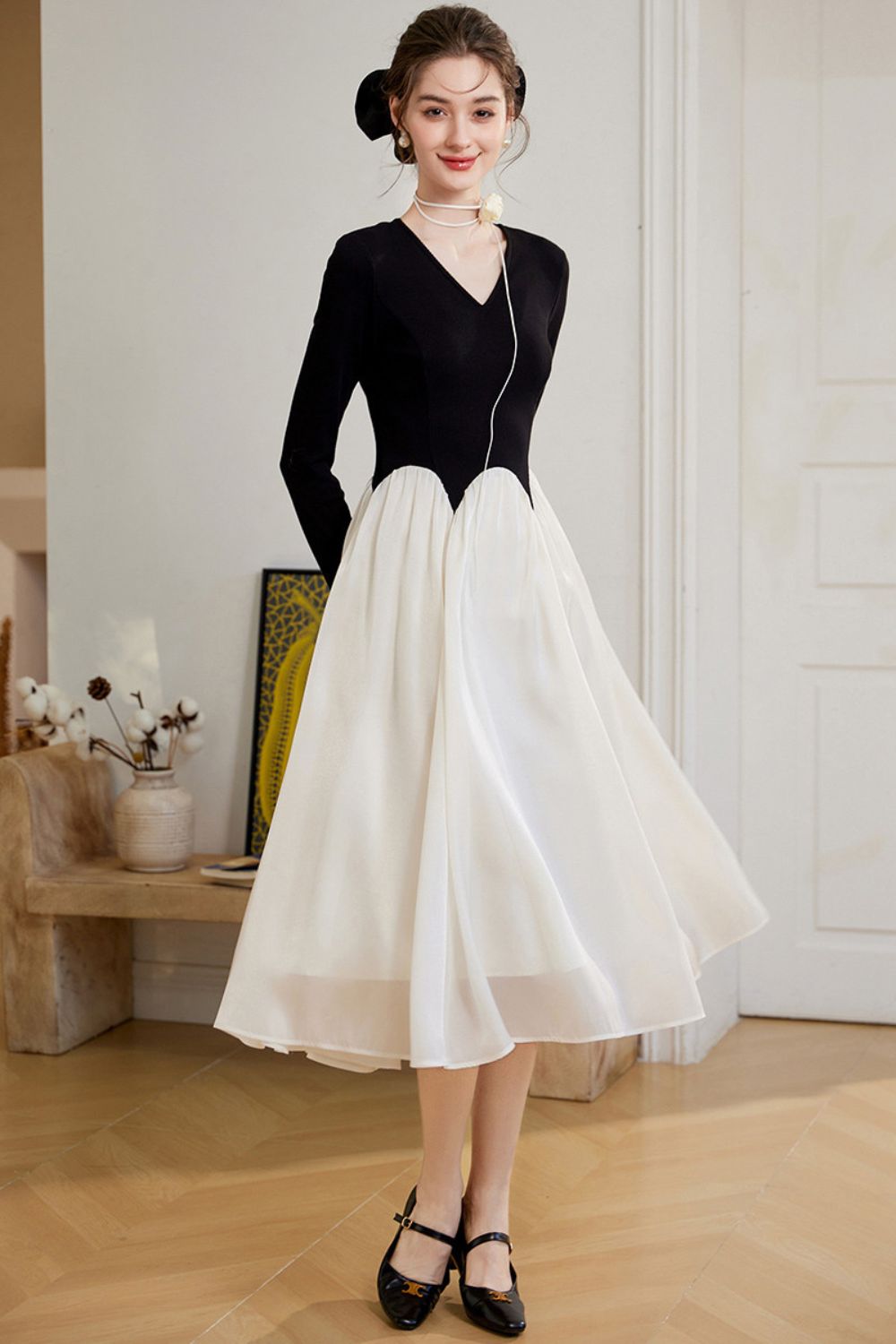 Model wearing a black long-sleeve top with a white flared midi skirt, standing in a room