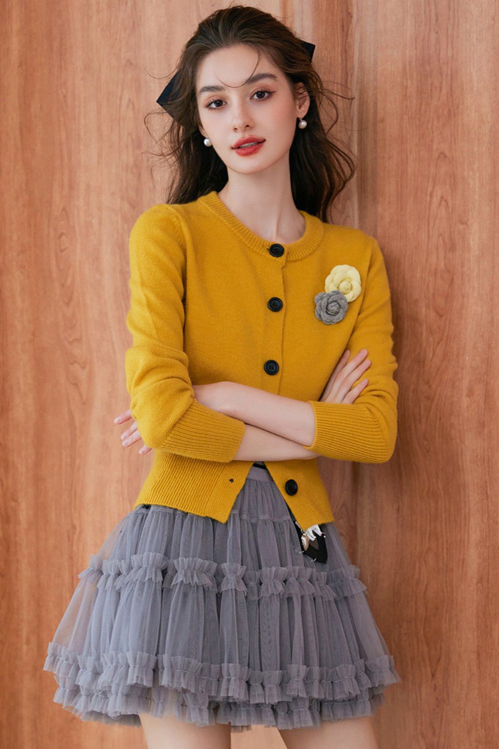 Front view of mustard yellow cardigan with flower detail and gray pleated skirt