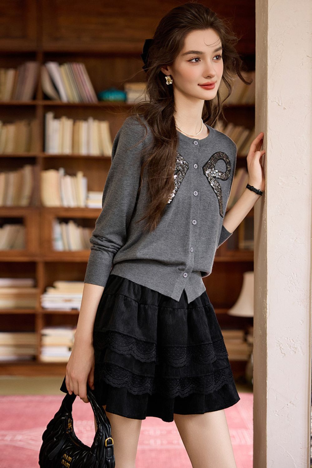 Side view of gray bow-embellished sweater styled with black ruffle mini skirt