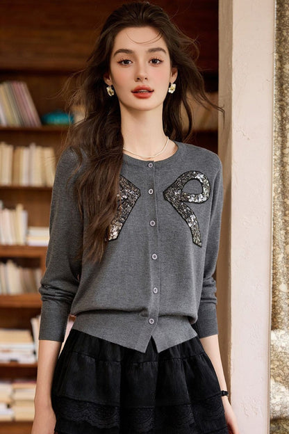 Front view of gray sweater with decorative bow accents and black layered skirt
