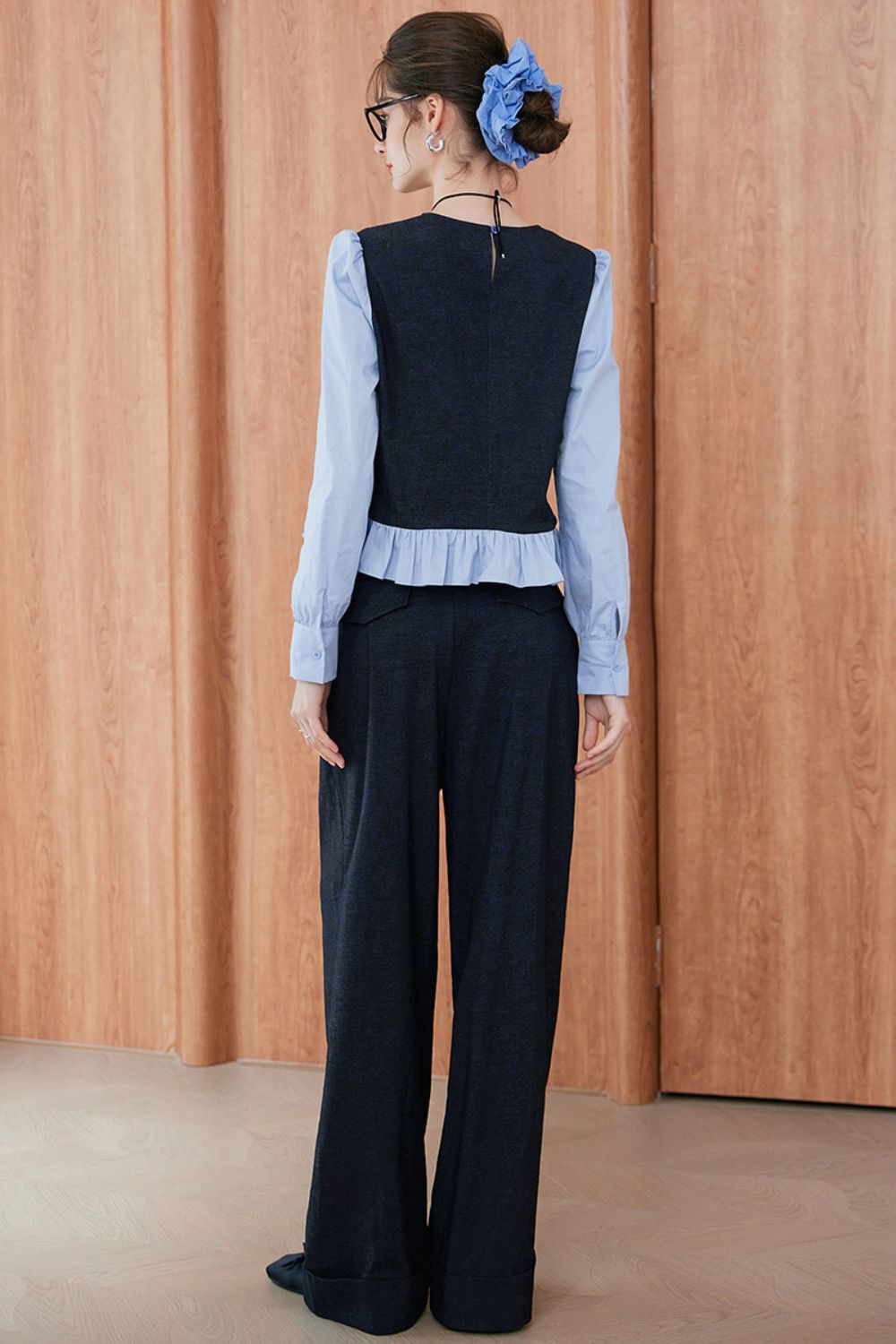 Rear view of navy blue sleeveless vest and wide-leg trousers layered over light blue blouse