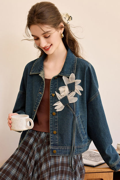 Close-up front view of woman in a denim jacket with white floral appliqué over a brown top and plaid skirt
