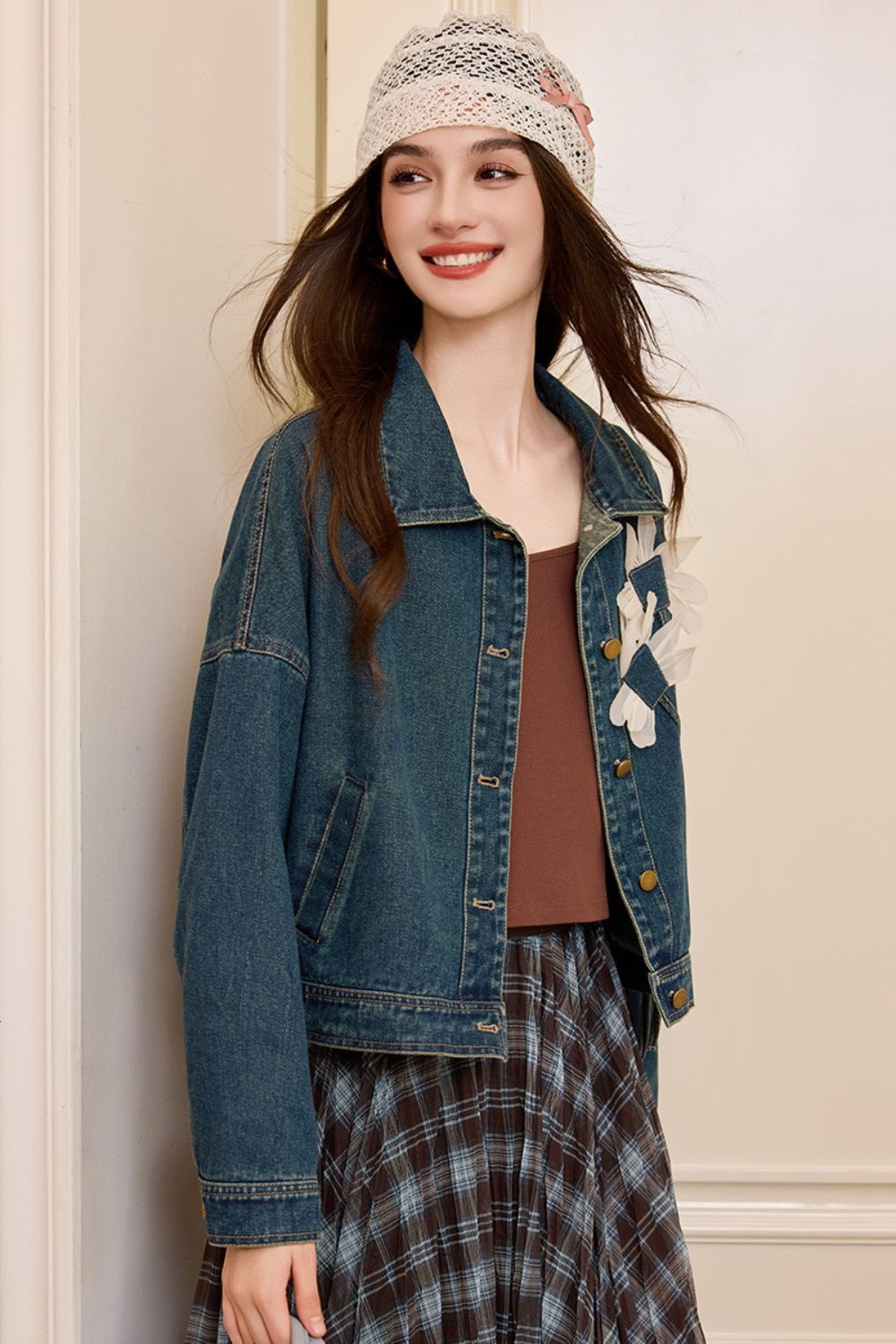 Side view of woman in denim jacket with floral appliqué and plaid skirt, wearing a knit beanie
