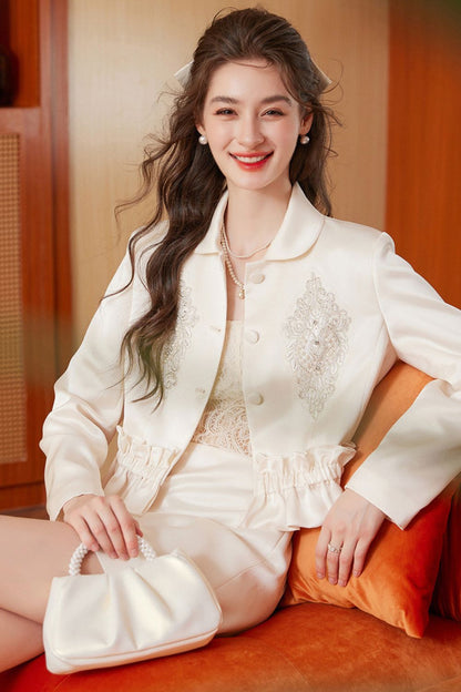 Smiling model in cream embroidered tassel jacket and cream mini skirt seated on a sofa