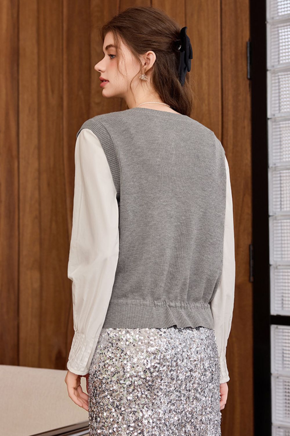 Back view of gray knit vest styled with a white blouse and floral skirt