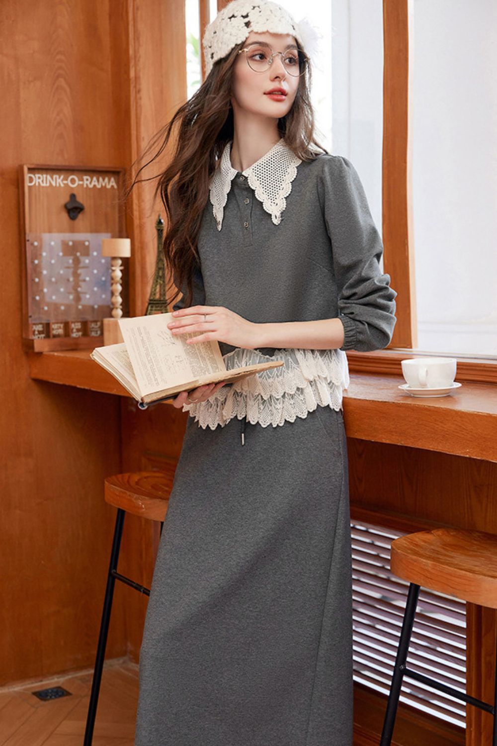 Model holding book, styled in gray lace-trimmed blouse and skirt with crochet hat