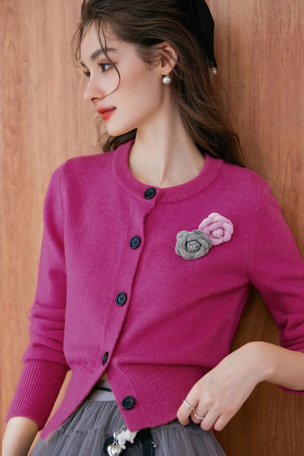 Close-up of model wearing a pink buttoned cardigan with floral brooch, paired with a gray pleated skirt.